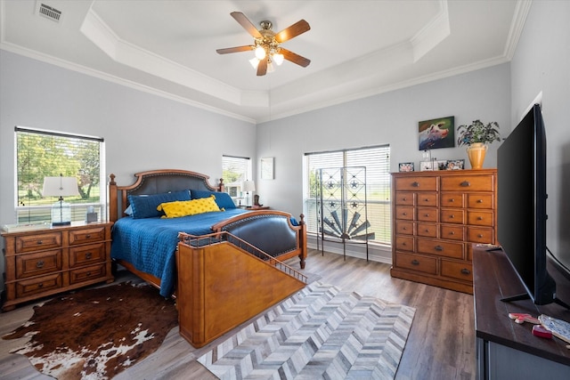 bedroom with ceiling fan, wood finished floors, visible vents, ornamental molding, and a tray ceiling