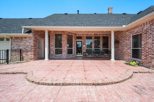 property entrance with a shingled roof, brick siding, and a patio