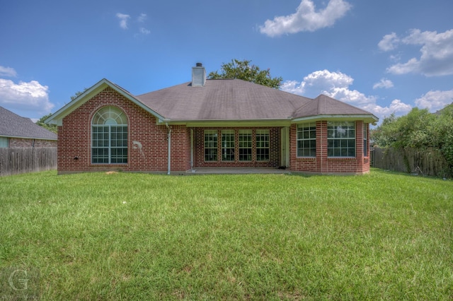 back of house featuring a shingled roof, a chimney, fence, a yard, and brick siding