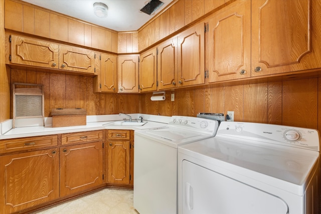 clothes washing area featuring separate washer and dryer, wood walls, sink, and cabinets