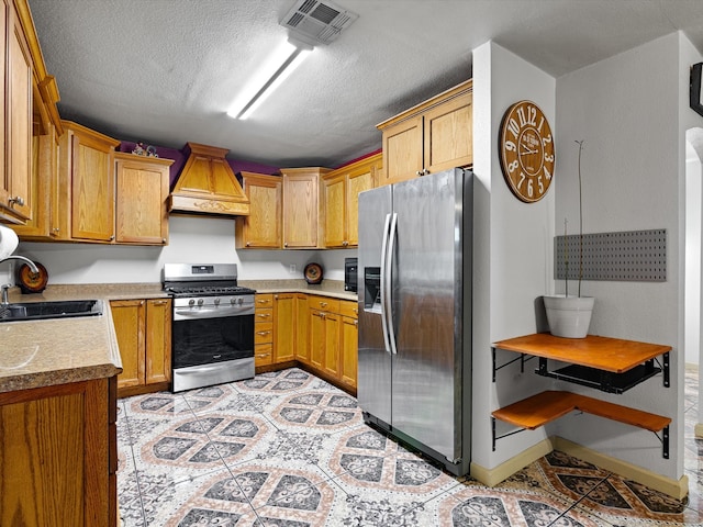 kitchen with custom exhaust hood, a textured ceiling, appliances with stainless steel finishes, light tile patterned floors, and sink