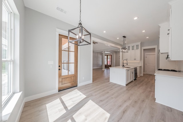 kitchen featuring decorative light fixtures, light countertops, white cabinets, a kitchen island with sink, and a sink