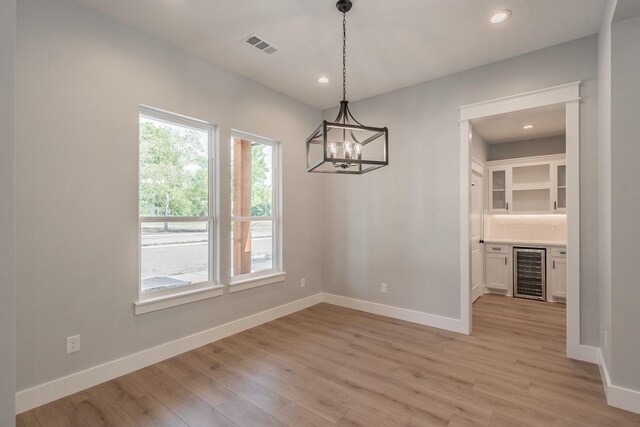 unfurnished dining area featuring light hardwood / wood-style flooring, a notable chandelier, and beverage cooler