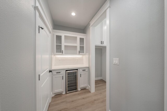 bar featuring tasteful backsplash, light wood-type flooring, beverage cooler, and white cabinetry