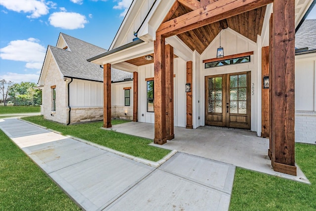 doorway to property with french doors, roof with shingles, a lawn, board and batten siding, and stone siding