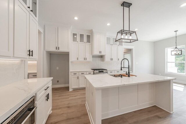 kitchen with tasteful backsplash, appliances with stainless steel finishes, an island with sink, light hardwood / wood-style flooring, and sink