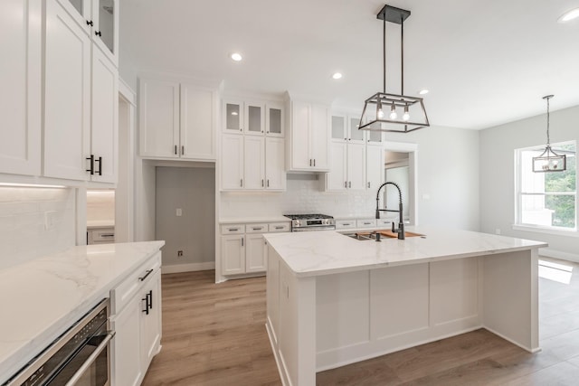 kitchen featuring a kitchen island with sink, a sink, glass insert cabinets, and light stone countertops