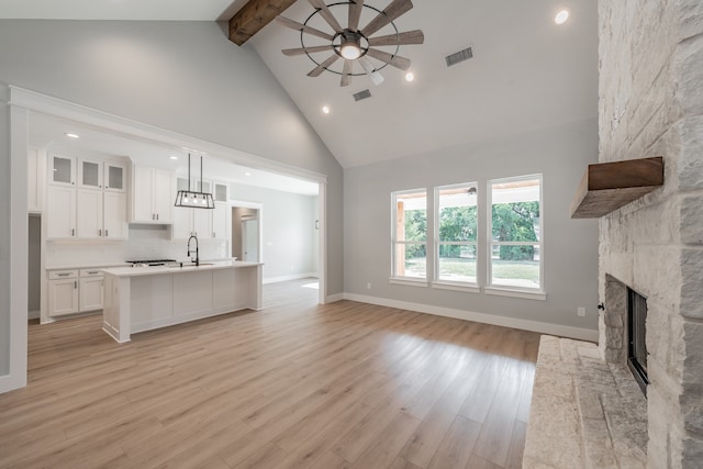 unfurnished living room featuring high vaulted ceiling, a fireplace, beam ceiling, and light hardwood / wood-style floors