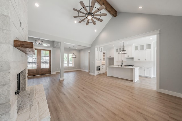 unfurnished living room with light wood-style floors, beamed ceiling, high vaulted ceiling, and a sink