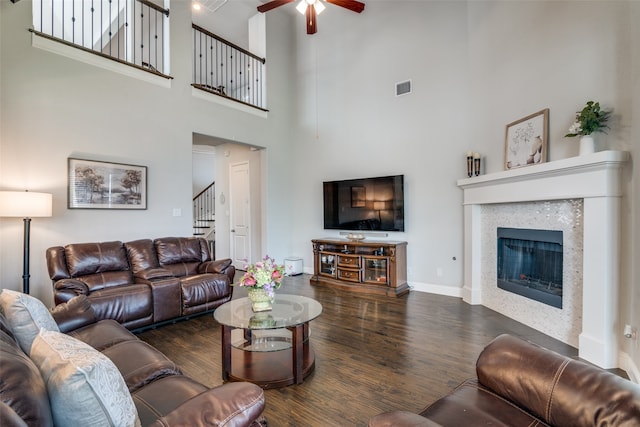 living room featuring ceiling fan, a fireplace, dark hardwood / wood-style floors, and a high ceiling