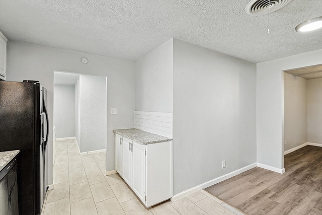 2120 Nottingham Blvd, Fort Worth, TX 76112 - kitchen with light hardwood / wood-style flooring, light stone countertops, white cabinets, black fridge, and decorative backsplash