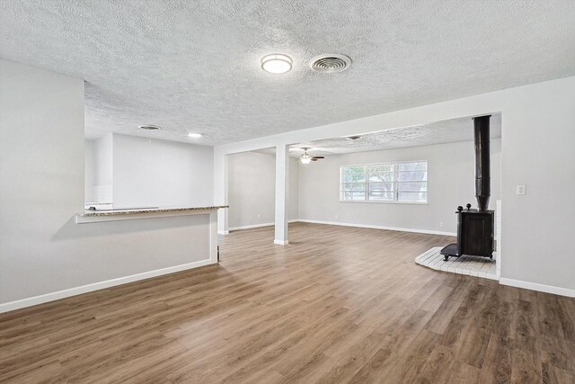 2120 Nottingham Blvd, Fort Worth, TX 76112 - unfurnished living room featuring hardwood / wood-style flooring, a textured ceiling, ceiling fan, and a wood stove