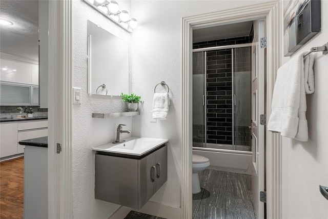 full bathroom with hardwood / wood-style floors, shower / bath combination with glass door, vanity, and toilet