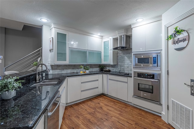 kitchen featuring white cabinets, wall chimney range hood, hardwood / wood-style flooring, stainless steel appliances, and decorative backsplash