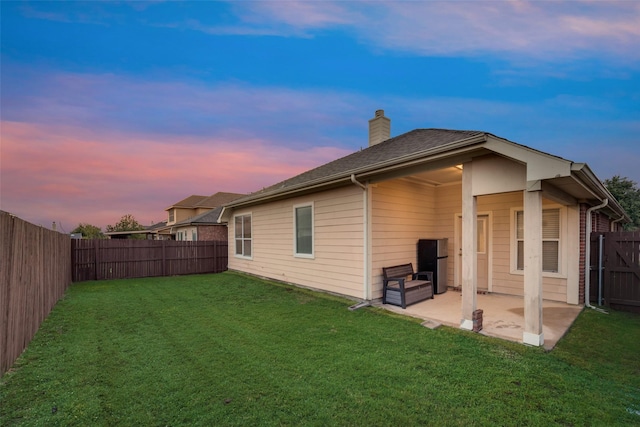 back house at dusk with a lawn and a patio area