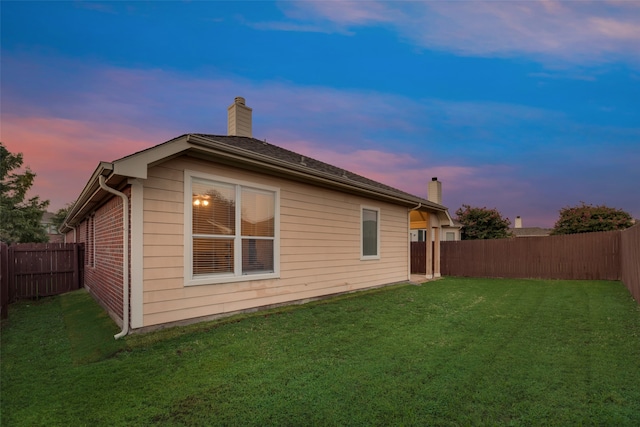 back house at dusk featuring a lawn