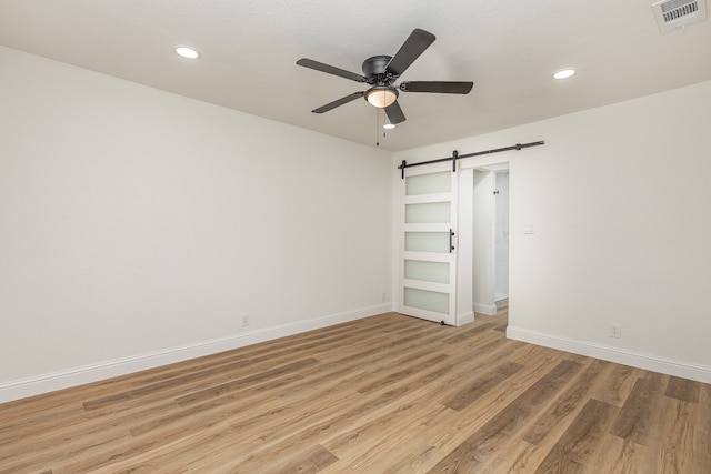 unfurnished bedroom with ceiling fan, light wood-type flooring, and a barn door