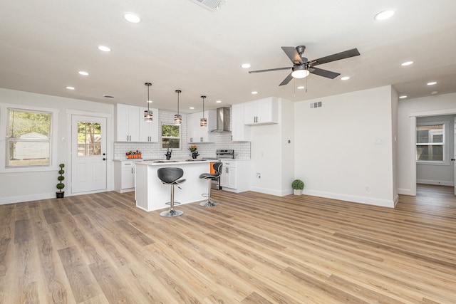 kitchen featuring a breakfast bar, ceiling fan, light hardwood / wood-style floors, a center island, and wall chimney range hood