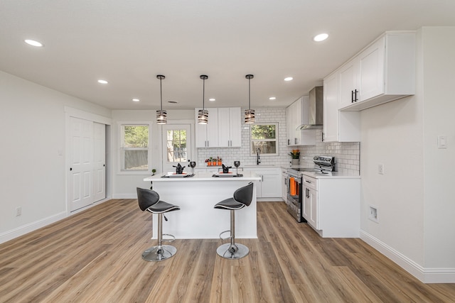 kitchen with wall chimney exhaust hood, range with electric stovetop, decorative light fixtures, light wood-type flooring, and a breakfast bar