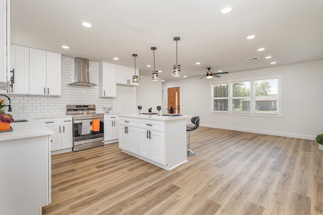 kitchen with stainless steel electric range oven, light wood-type flooring, white cabinetry, and wall chimney range hood