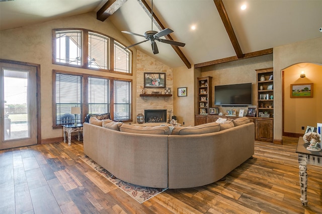 living room with a stone fireplace, dark hardwood / wood-style floors, high vaulted ceiling, ceiling fan, and beam ceiling