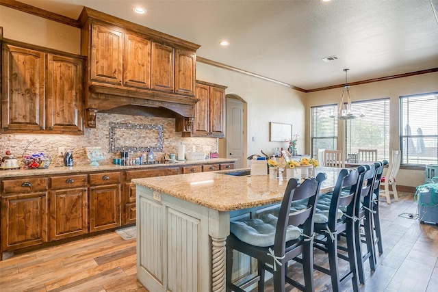 kitchen featuring backsplash, a kitchen breakfast bar, decorative light fixtures, and a kitchen island with sink