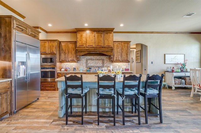 kitchen with decorative backsplash, hardwood / wood-style floors, a breakfast bar, built in appliances, and a kitchen island