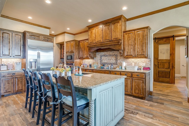 kitchen with tasteful backsplash, a kitchen island with sink, hardwood / wood-style flooring, and built in appliances