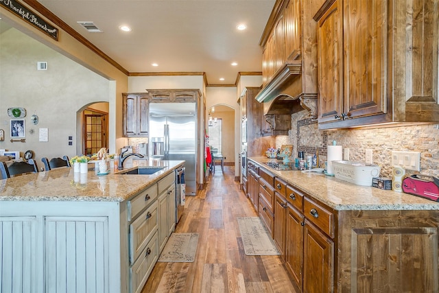 kitchen with decorative backsplash, a kitchen island with sink, crown molding, hardwood / wood-style flooring, and sink