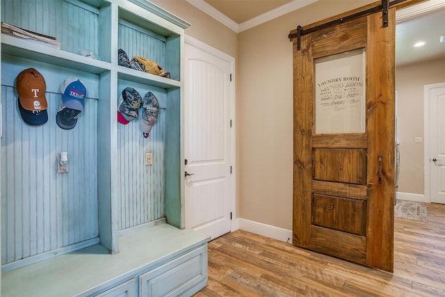 mudroom with a barn door, hardwood / wood-style flooring, and crown molding