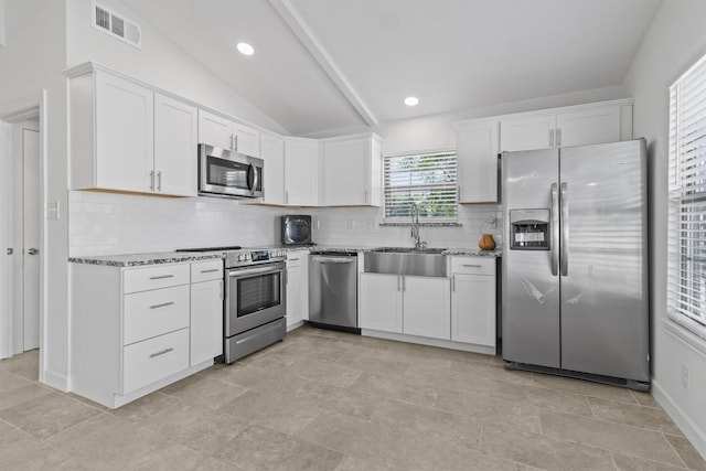 kitchen with white cabinetry, appliances with stainless steel finishes, light stone countertops, and vaulted ceiling