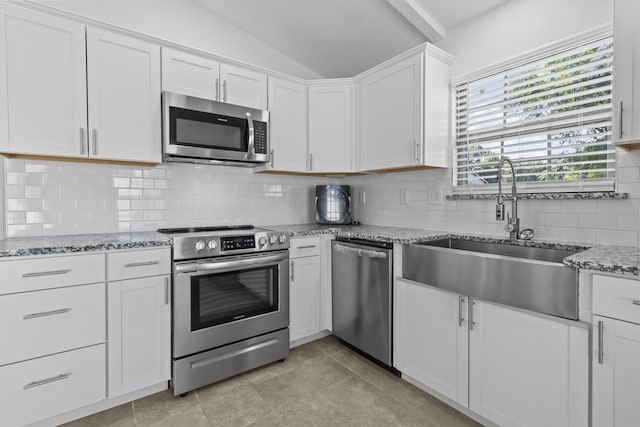 kitchen with tasteful backsplash, appliances with stainless steel finishes, lofted ceiling, white cabinetry, and light tile patterned floors