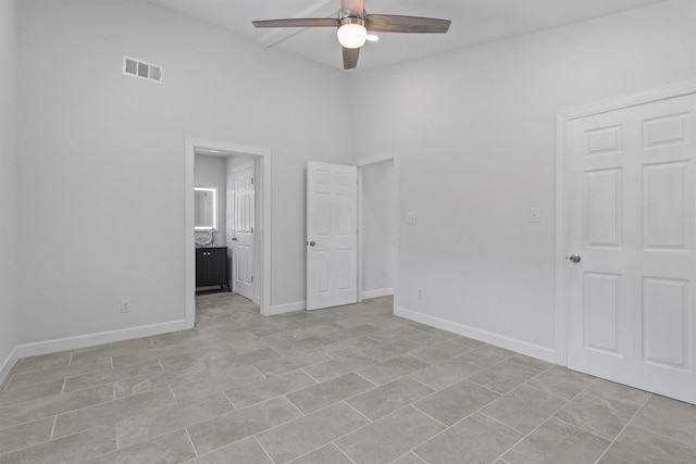 unfurnished bedroom with baseboards, visible vents, ceiling fan, ensuite bathroom, and a high ceiling