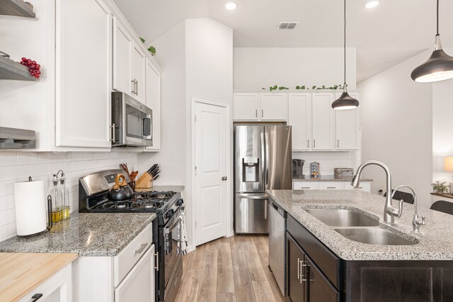 kitchen with a kitchen island with sink, white cabinetry, sink, appliances with stainless steel finishes, and light hardwood / wood-style floors