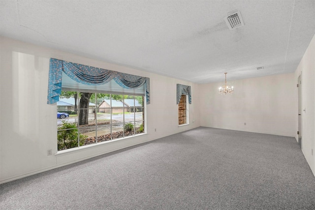 carpeted empty room featuring visible vents, a textured ceiling, and an inviting chandelier