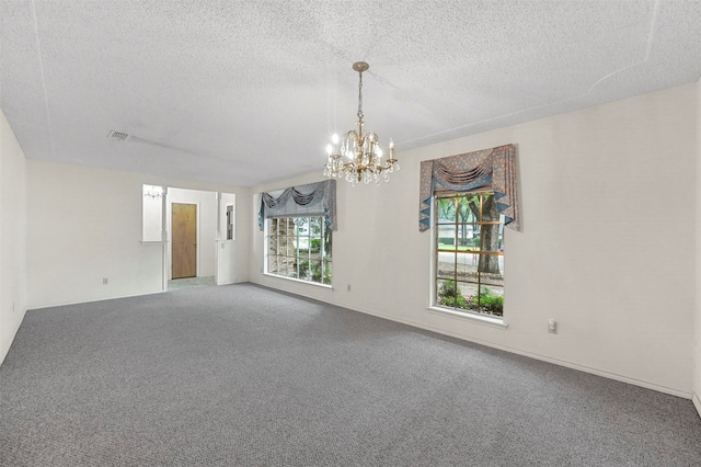 carpeted empty room featuring a notable chandelier, a textured ceiling, and a wealth of natural light