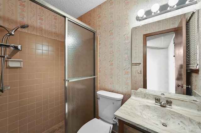 bathroom with vanity, wallpapered walls, a shower stall, a textured ceiling, and toilet