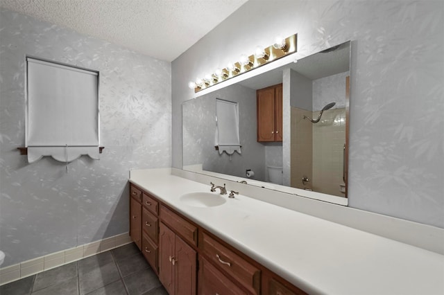 bathroom with vanity, tile patterned flooring, toilet, tiled shower, and a textured ceiling