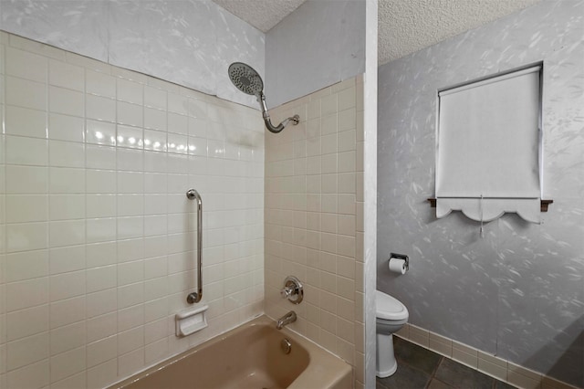 bathroom featuring tile patterned floors, toilet, a textured ceiling, and tiled shower / bath