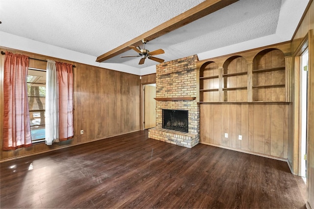 unfurnished living room with a brick fireplace, wooden walls, dark wood-type flooring, and a textured ceiling