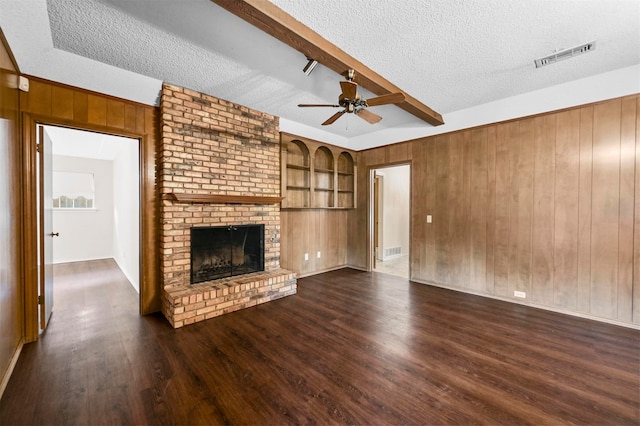 unfurnished living room featuring a fireplace, beamed ceiling, dark wood-type flooring, and a textured ceiling