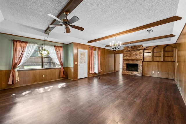 unfurnished living room featuring visible vents, beamed ceiling, wood walls, wood finished floors, and a textured ceiling