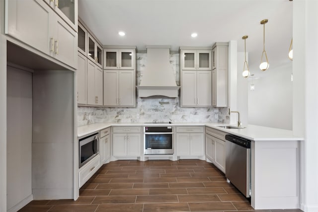 kitchen with stainless steel appliances, custom exhaust hood, sink, tasteful backsplash, and decorative light fixtures