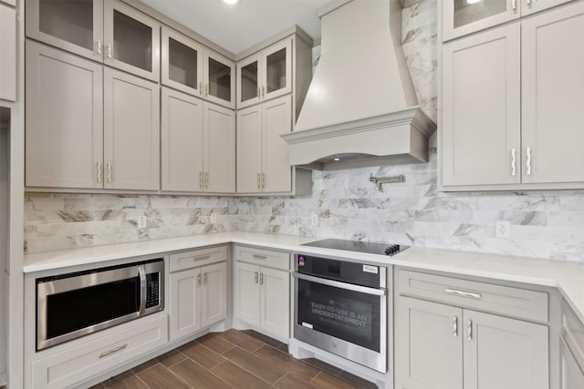 kitchen with dark hardwood / wood-style flooring, custom range hood, appliances with stainless steel finishes, backsplash, and white cabinetry