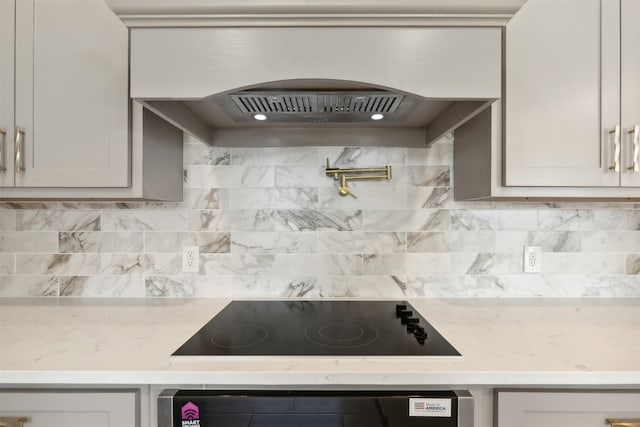 kitchen with backsplash, wall oven, light stone counters, custom range hood, and black electric stovetop