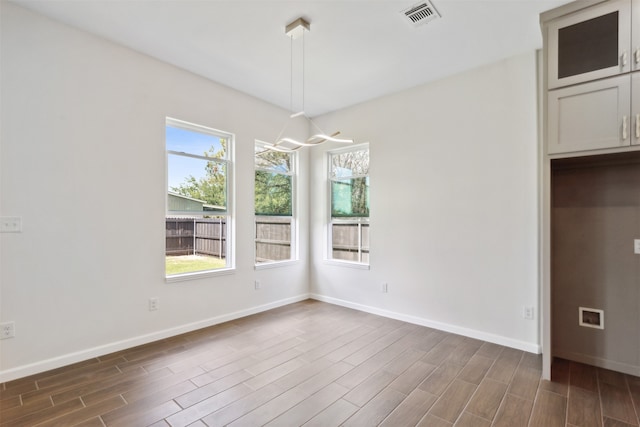 unfurnished dining area with a notable chandelier, hardwood / wood-style flooring, and a healthy amount of sunlight