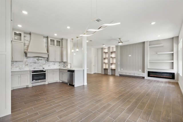 kitchen with pendant lighting, appliances with stainless steel finishes, ceiling fan, wood-type flooring, and custom range hood