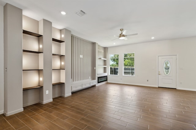 unfurnished living room featuring ceiling fan and built in shelves