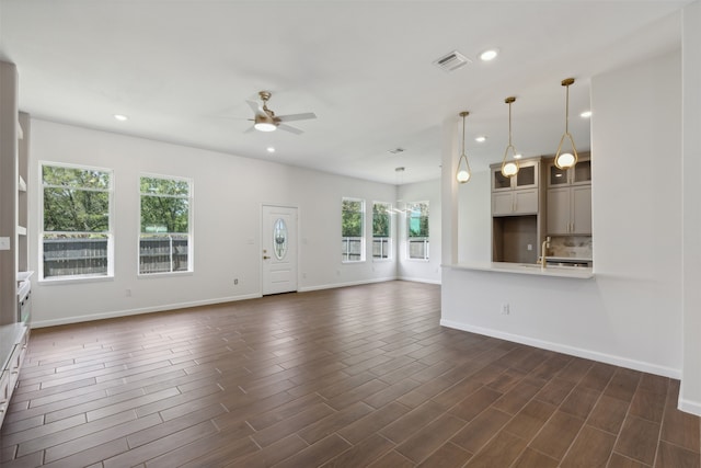 unfurnished living room featuring ceiling fan, dark hardwood / wood-style floors, and a healthy amount of sunlight