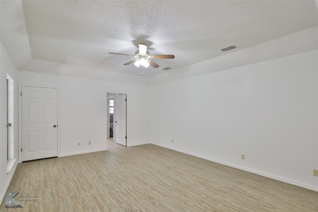 spare room with a textured ceiling, a raised ceiling, ceiling fan, and light hardwood / wood-style floors